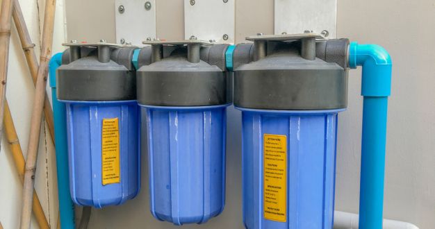 Tres filtros de agua azules conectados mediante tuberías en una pared